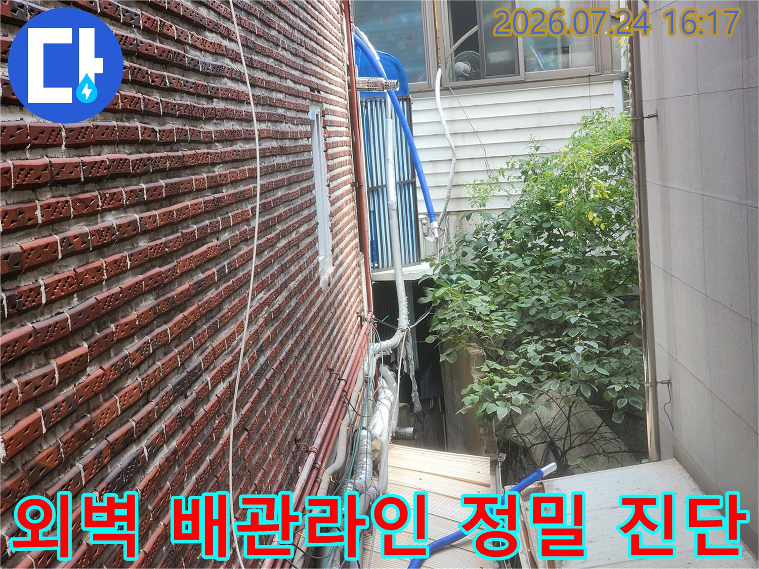 붉은 벽돌 건물 외벽과 파란색 보온재로 감싼 수도 배관 시스템 점검