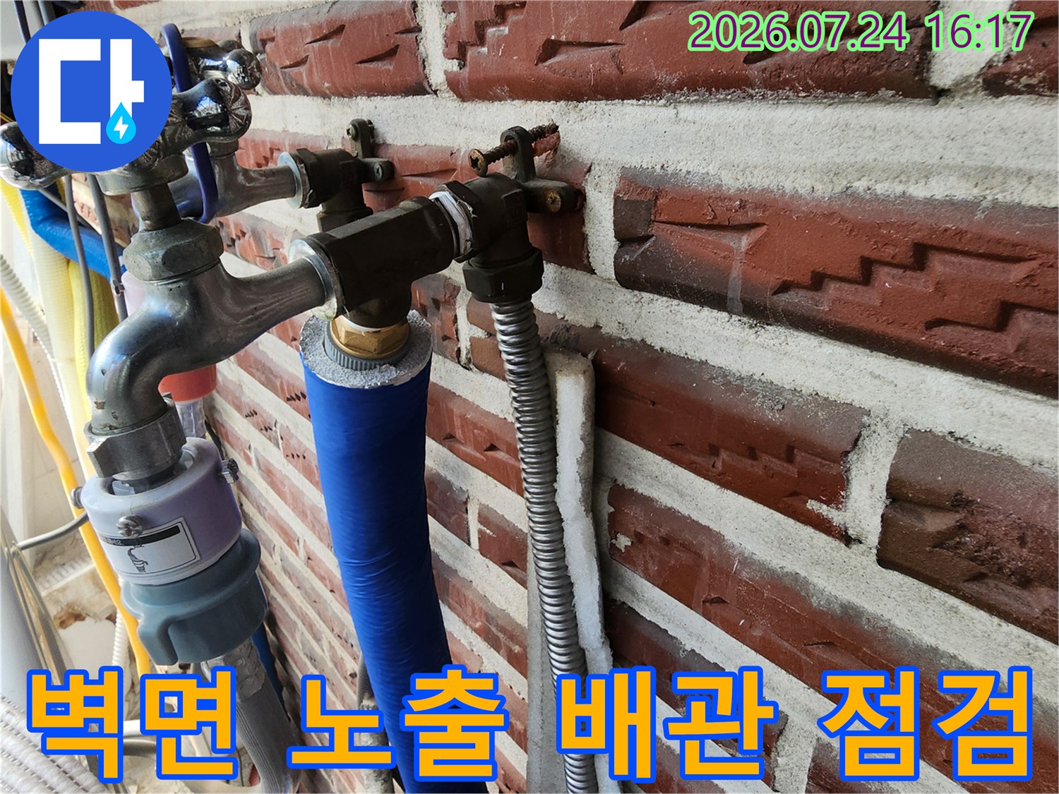 붉은 벽돌 외벽에 고정된 파란색과 은색 단열재로 감싸진 수도배관 라인