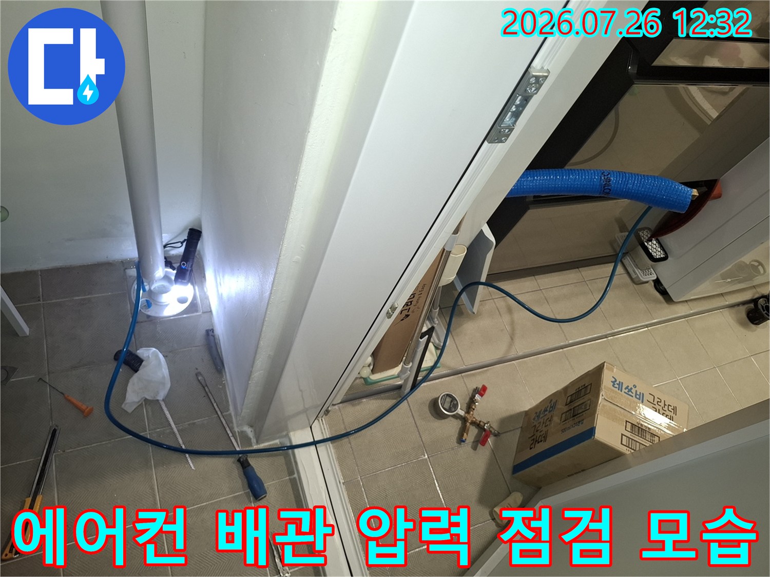 다용도실 바닥에서 파란색 호스와 공압 테스트 장비를 연결하여 누수를 점검하는 모습