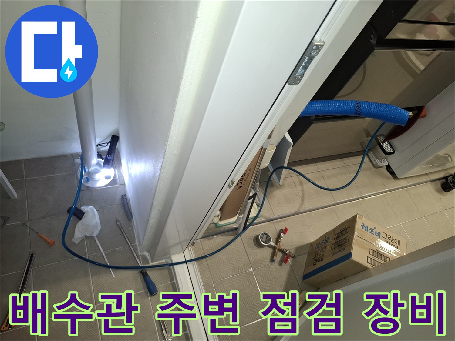 세탁실 바닥 타일 위로 설치된 배관 점검용 호스와 수공구들