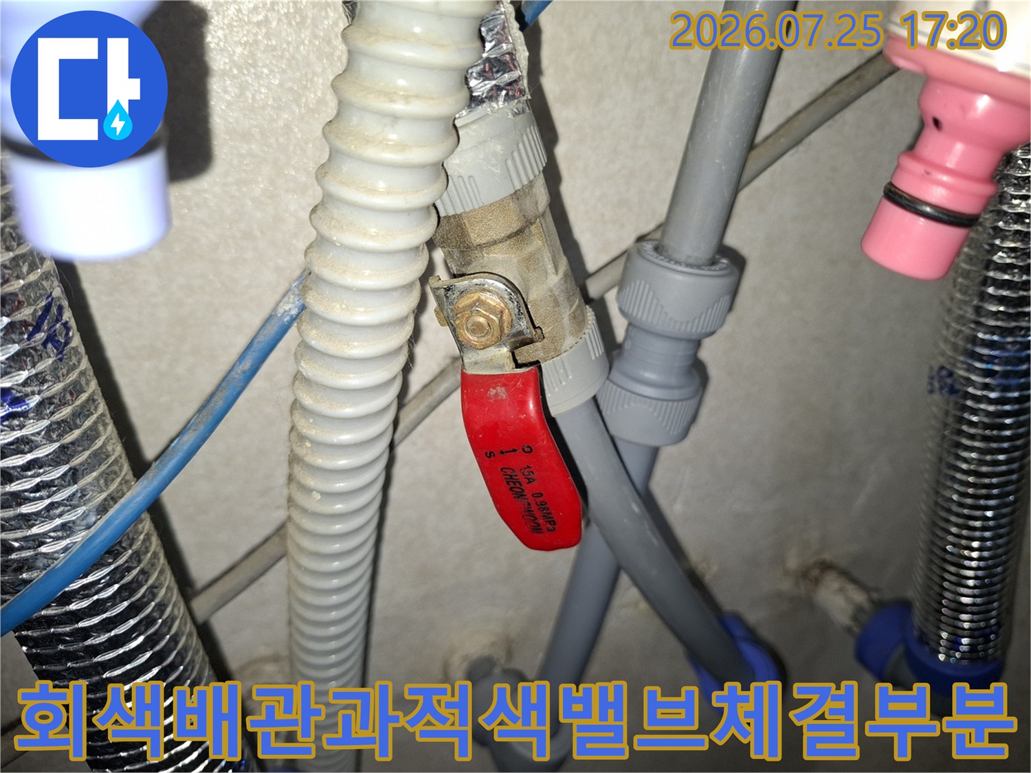 금속 너트로 고정된 적색 밸브 핸들과 회색 플라스틱 배관의 연결 접합부 상세 사진