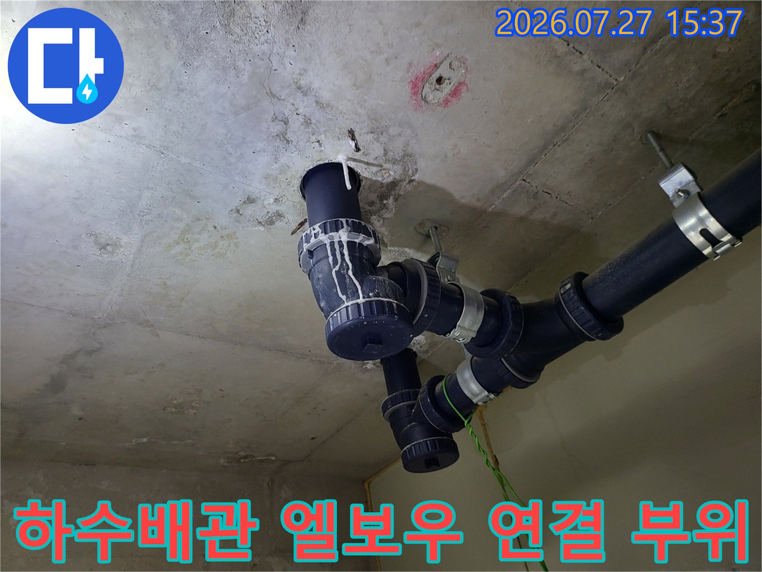 천장 콘크리트 면에 밀착되어 설치된 검은색 하수 배관과 고정 밴드