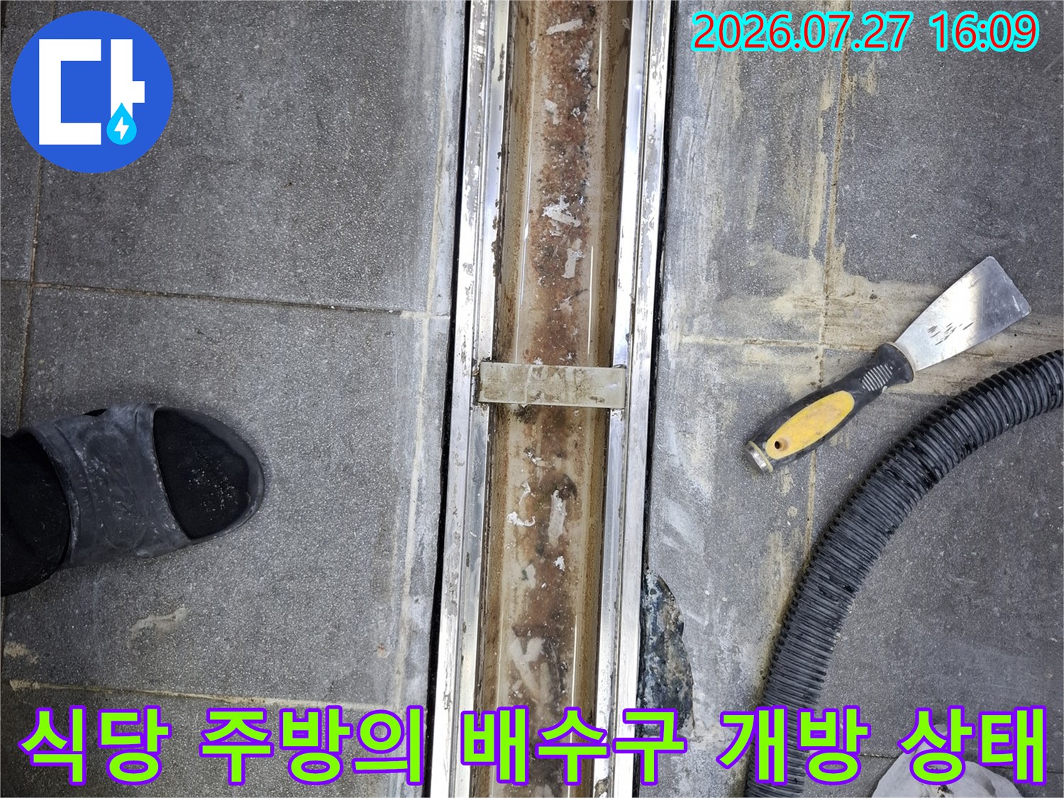 금속-트랜치의 덮개가 제거된 채로 내부가 드러나 있고 주변에 검은 호스가 놓인 모습