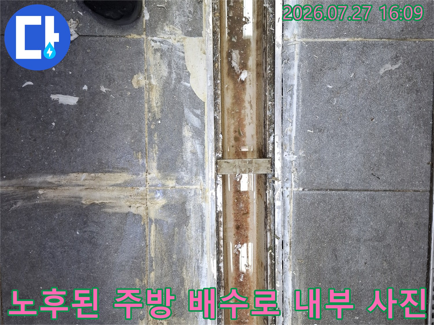 길쭉한 형태의 금속제 배수 트랜치가 설치되어 있으며 주변 타일 마감이 낡은 모습