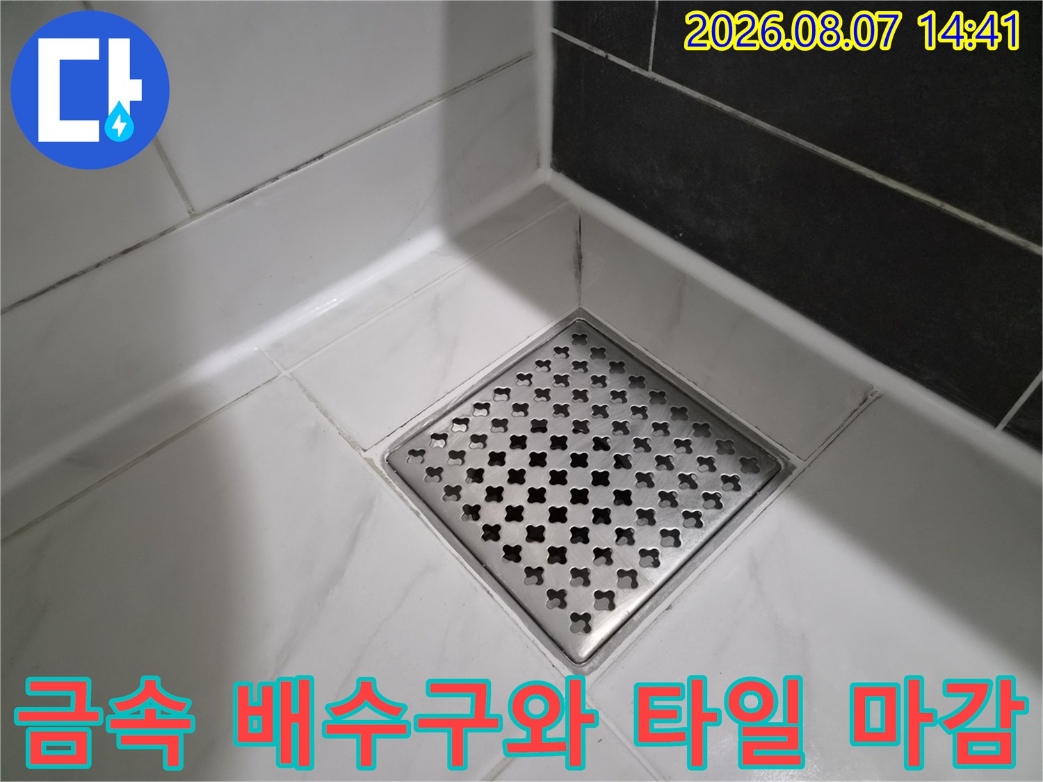 스테인리스 재질의 사각 배수구와 흰색 타일입니다.