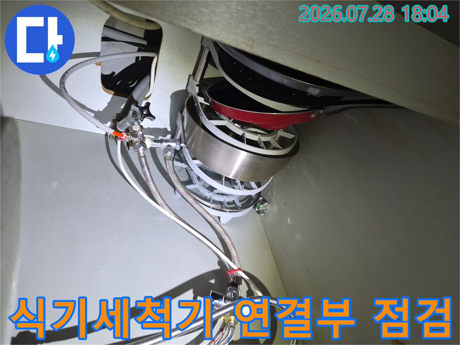 싱크대 하부장에서 식기세척기 급수 밸브와 호스들이 얽힌 구간을 살피는 장면입니다.