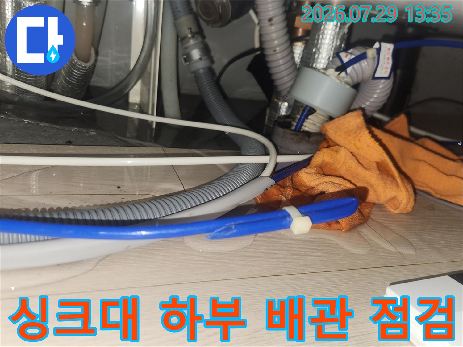 싱크대 아래쪽 노출된 회색 배관과 파란색 호스가 연결된 모습