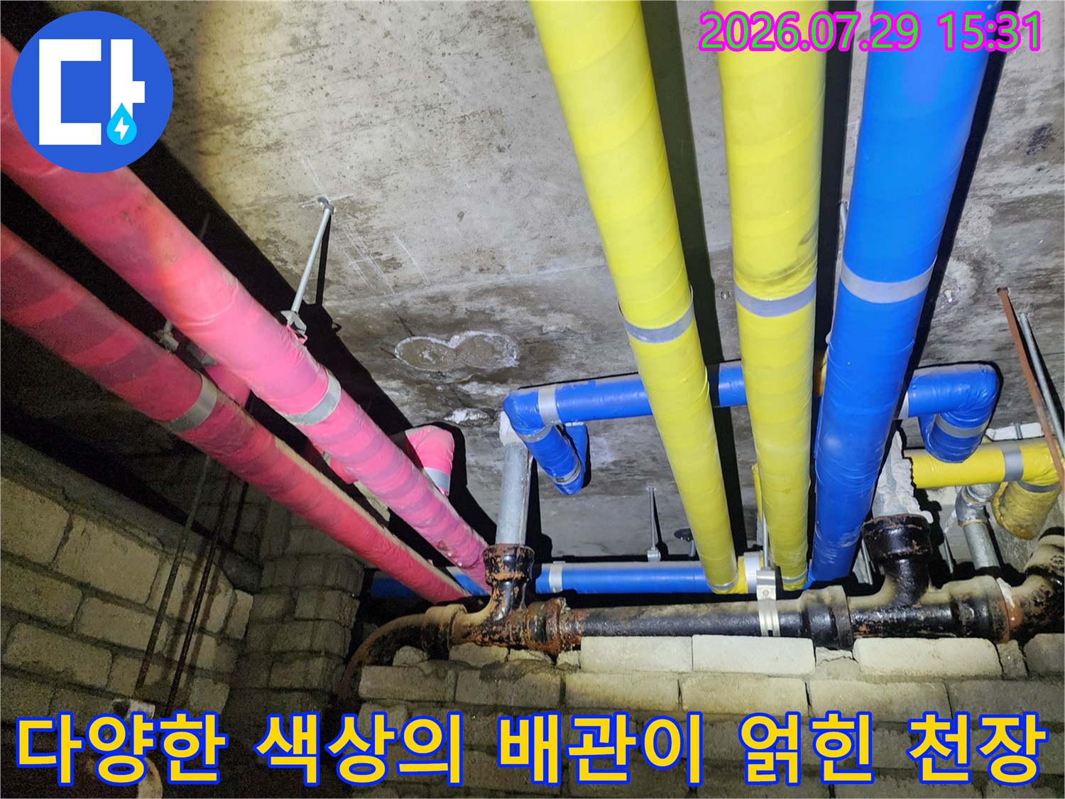천장 속에 배치된 노란색과 분홍색 및 파란색 보온재를 감싼 여러 개의 배관들