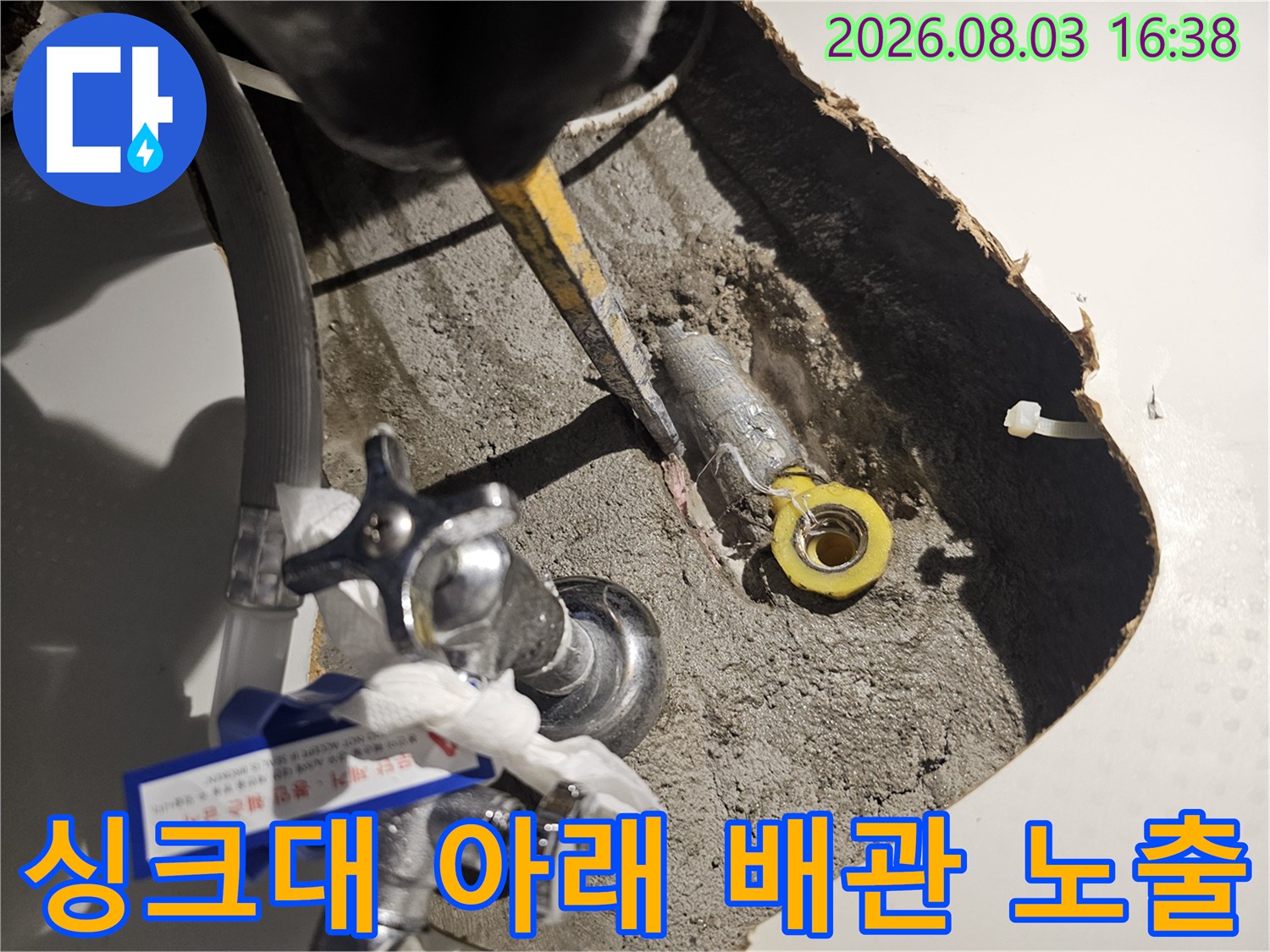 싱크대 하부 공간에 노출된 회색 및 노란색 배관 연결 부위