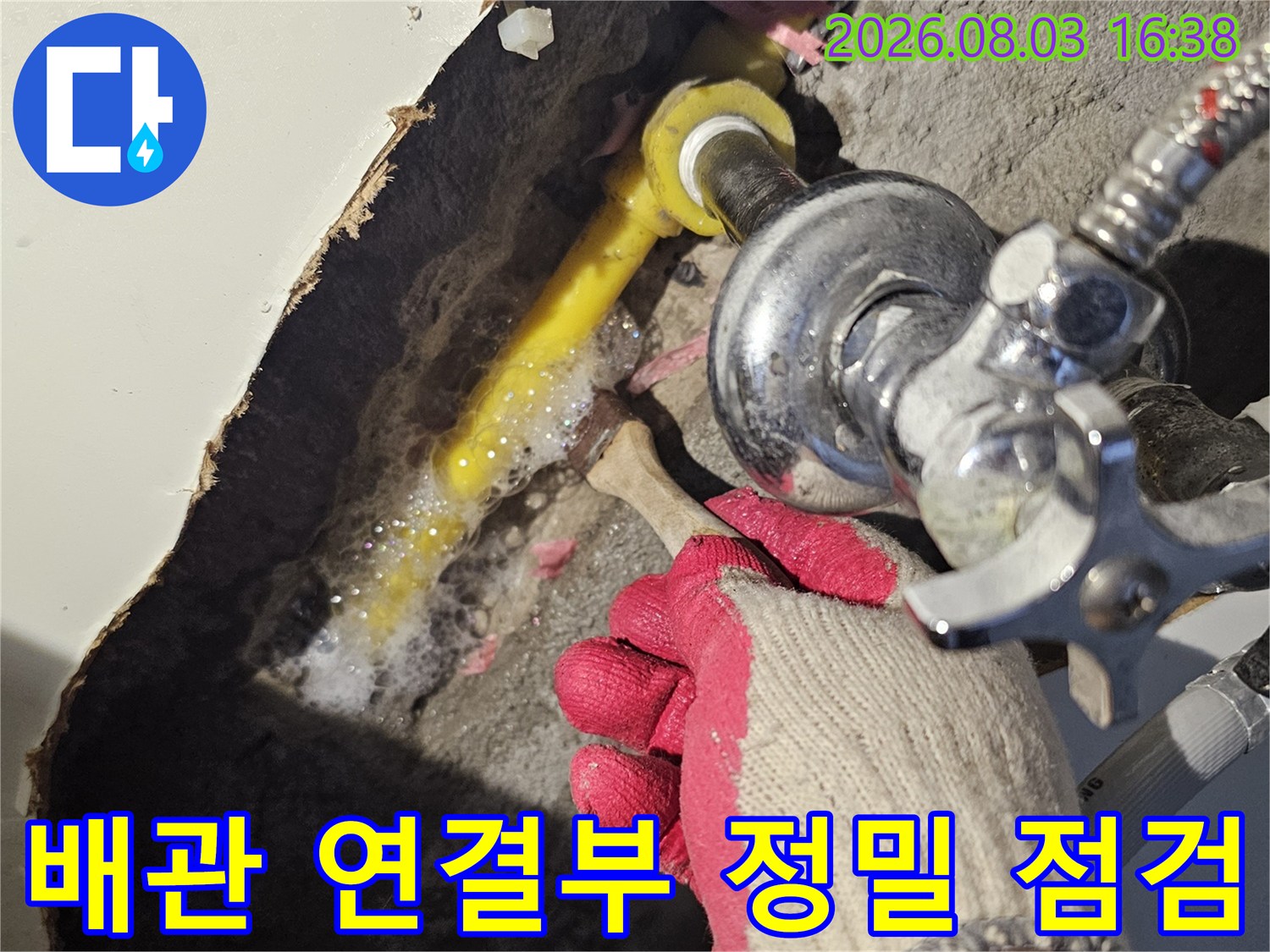장갑을 낀 작업자가 싱크대 아래 노출된 배관을 세심하게 살피는 모습