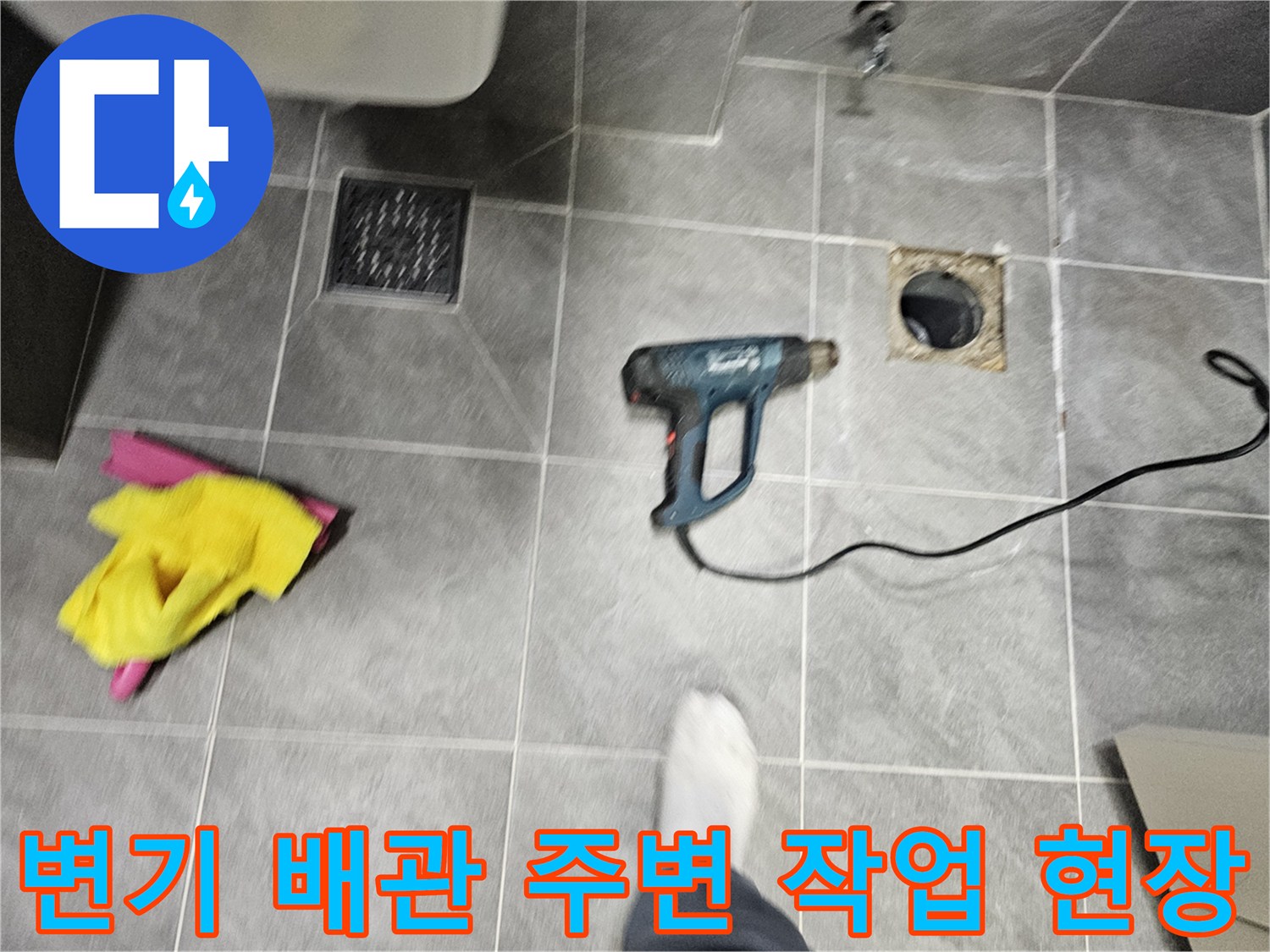 작업용 드릴과 청소 도구가 놓인 화장실 바닥 배관 부위