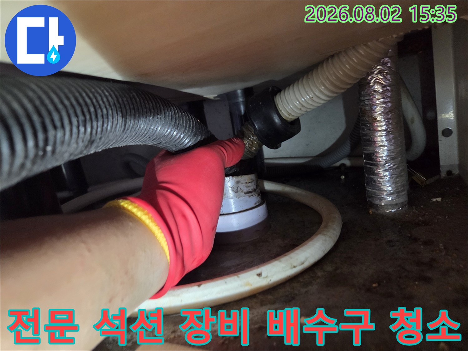 빨간색 작업용 장갑을 낀 엔지니어가 싱크대 아래 배수 관로에 석션 호스를 연결한 상태