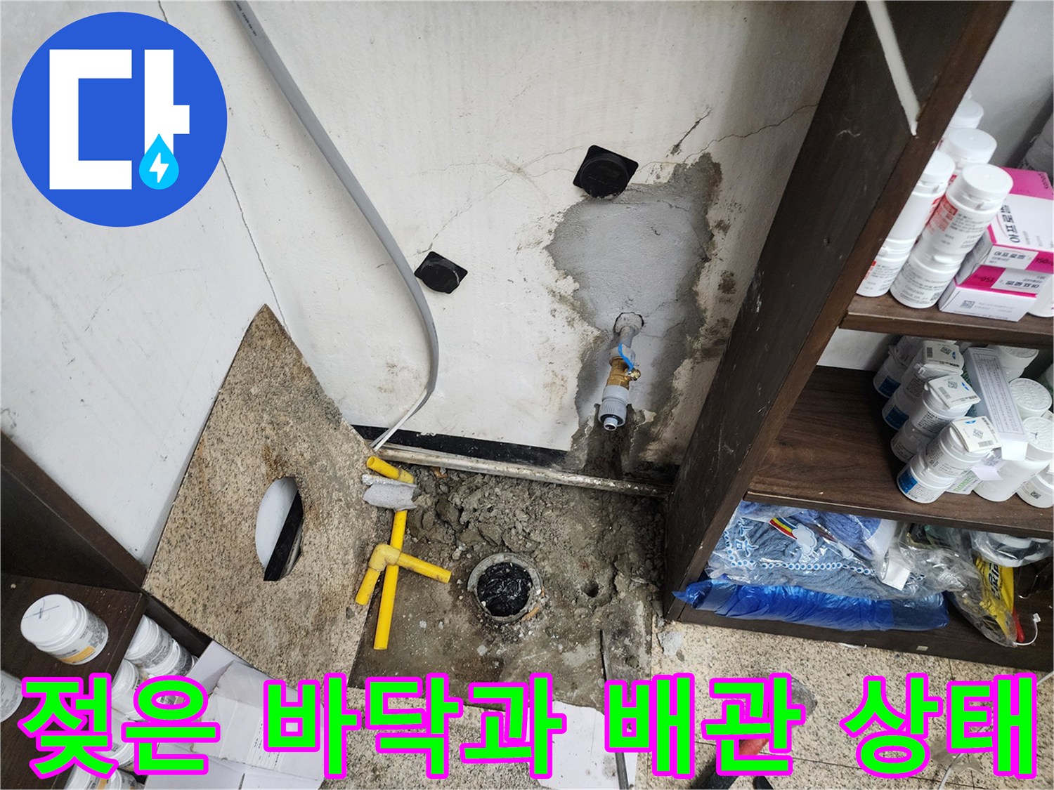 싱크대 밑부분의 젖은 바닥과 벽면 배관 연결 부위의 결함을 보여줍니다.