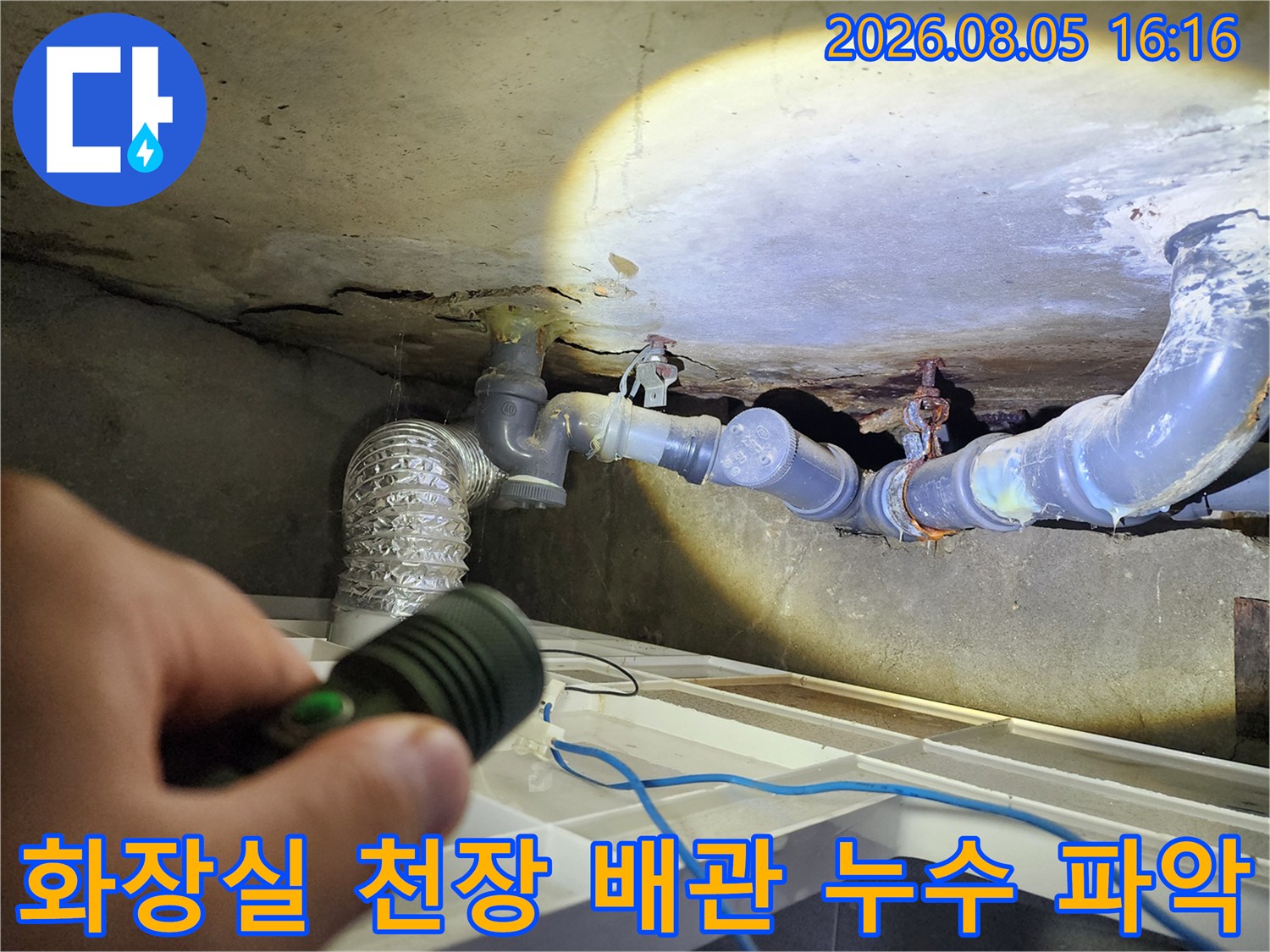 손전등으로 비춘 화장실 천장의 노출된 배관 부위 검사