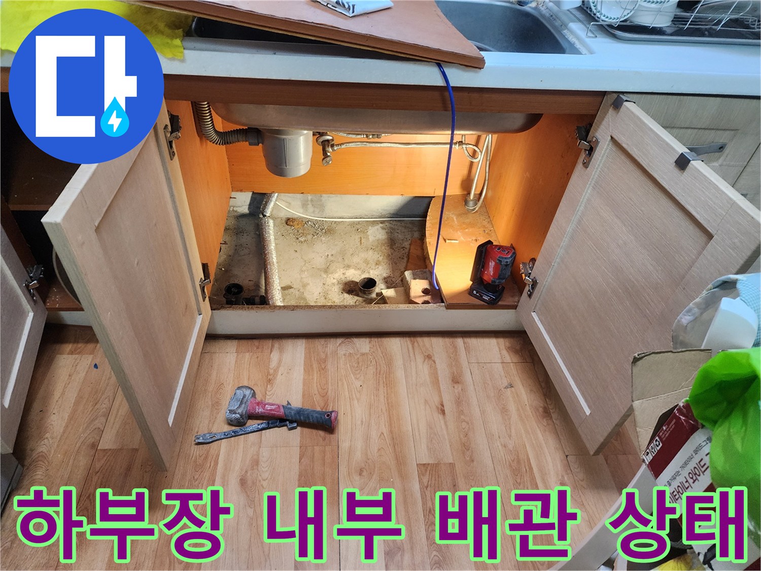 싱크대 하부장 아래쪽 노출된 배수관과 작업 도구