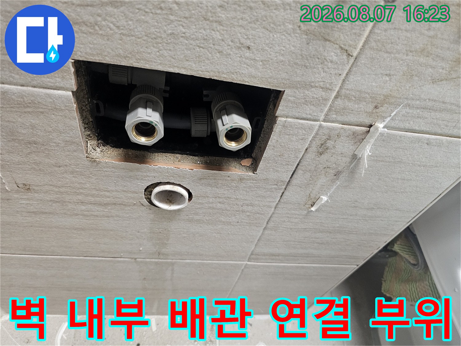 타일을 걷어내고 노출시킨 세면대 급수 배관 및 연결 부품입니다.