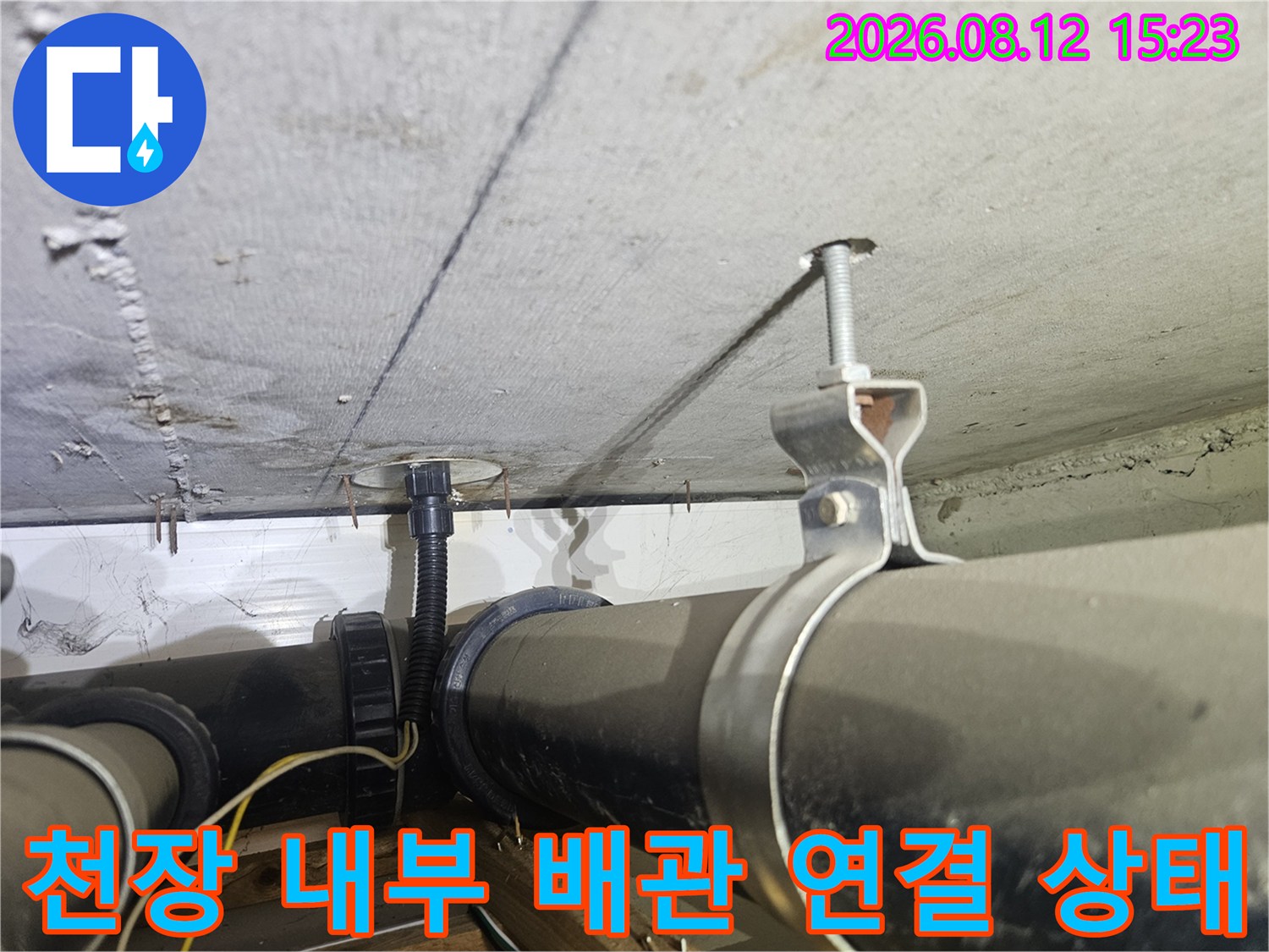 콘크리트 천장에 고정된 검은색 배수 배관과 전선관-연결 부위 모습