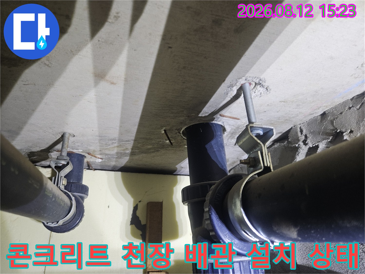 회색 콘크리트 천장에 고정된 검은색 플라스틱 하수 배관의 상세 모습