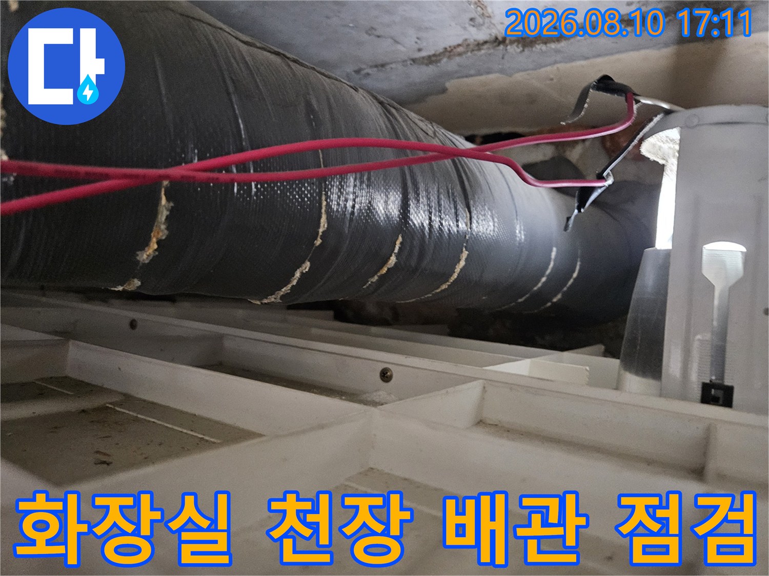 아파트 화장실 천장 구조물 아래로 지나가는 배관과 검사 장비 모습입니다.