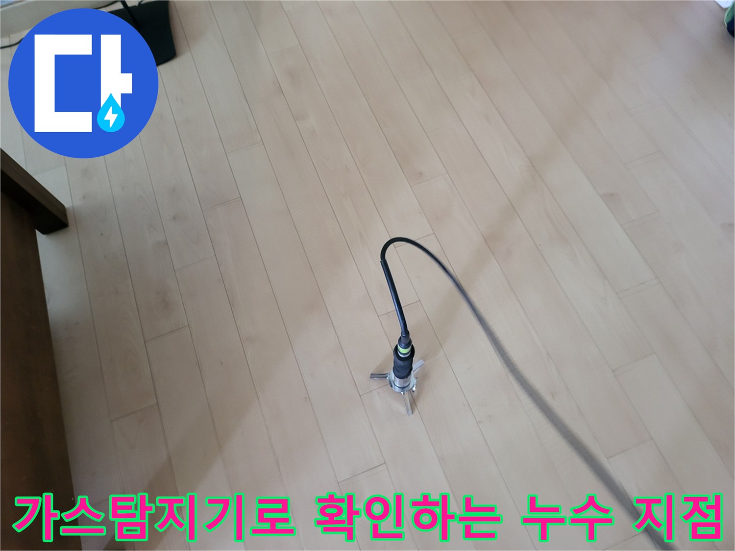 거실 나무 바닥 위에서 가스 탐지기를 활용하여 배관의 이상 여부를 정밀하게 점검하고 있습니다.