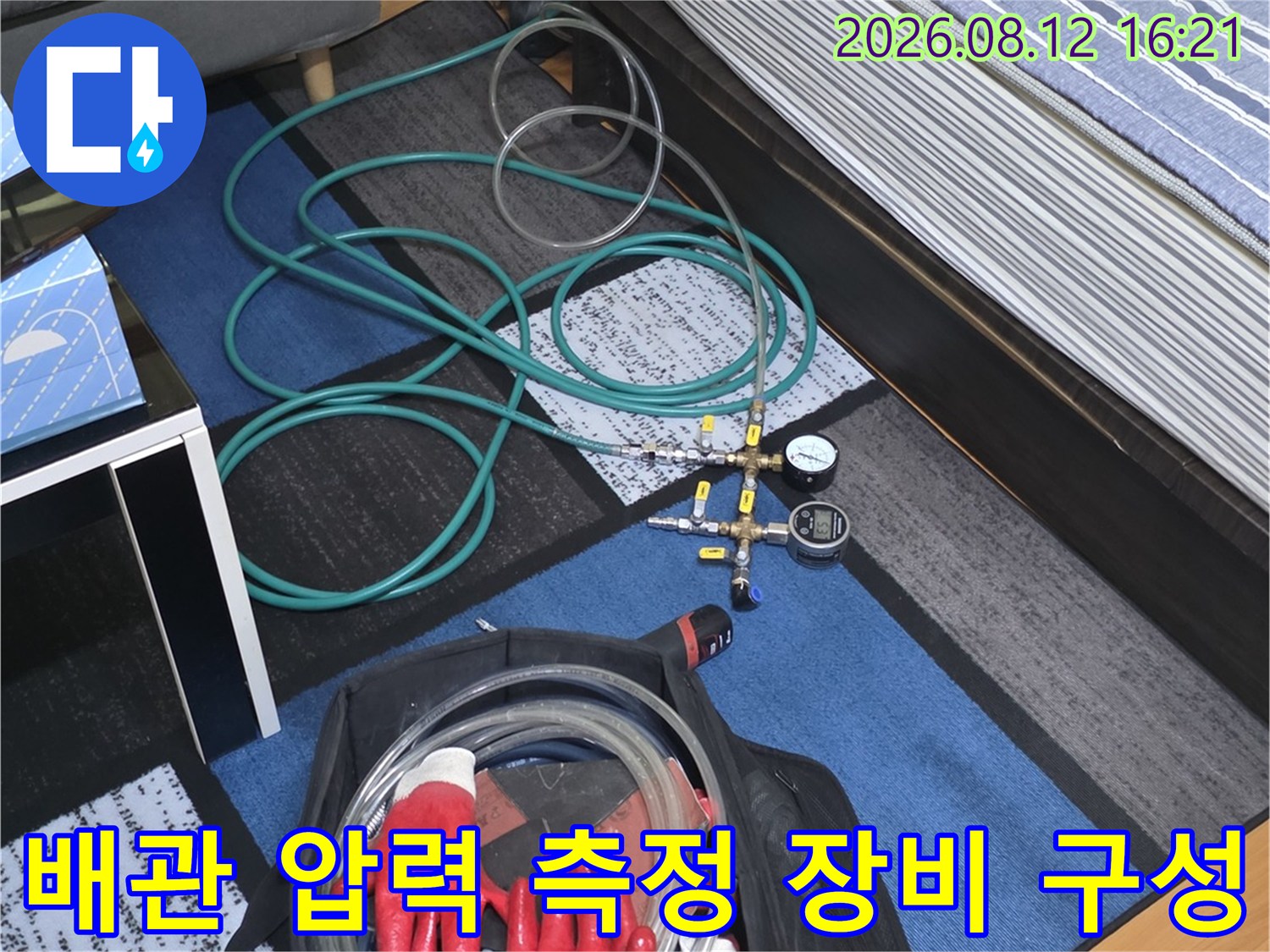 검은색 가방과 빨간색 작업 장갑 옆에 펼쳐진 청록색 누수 탐지용 호스-압력계