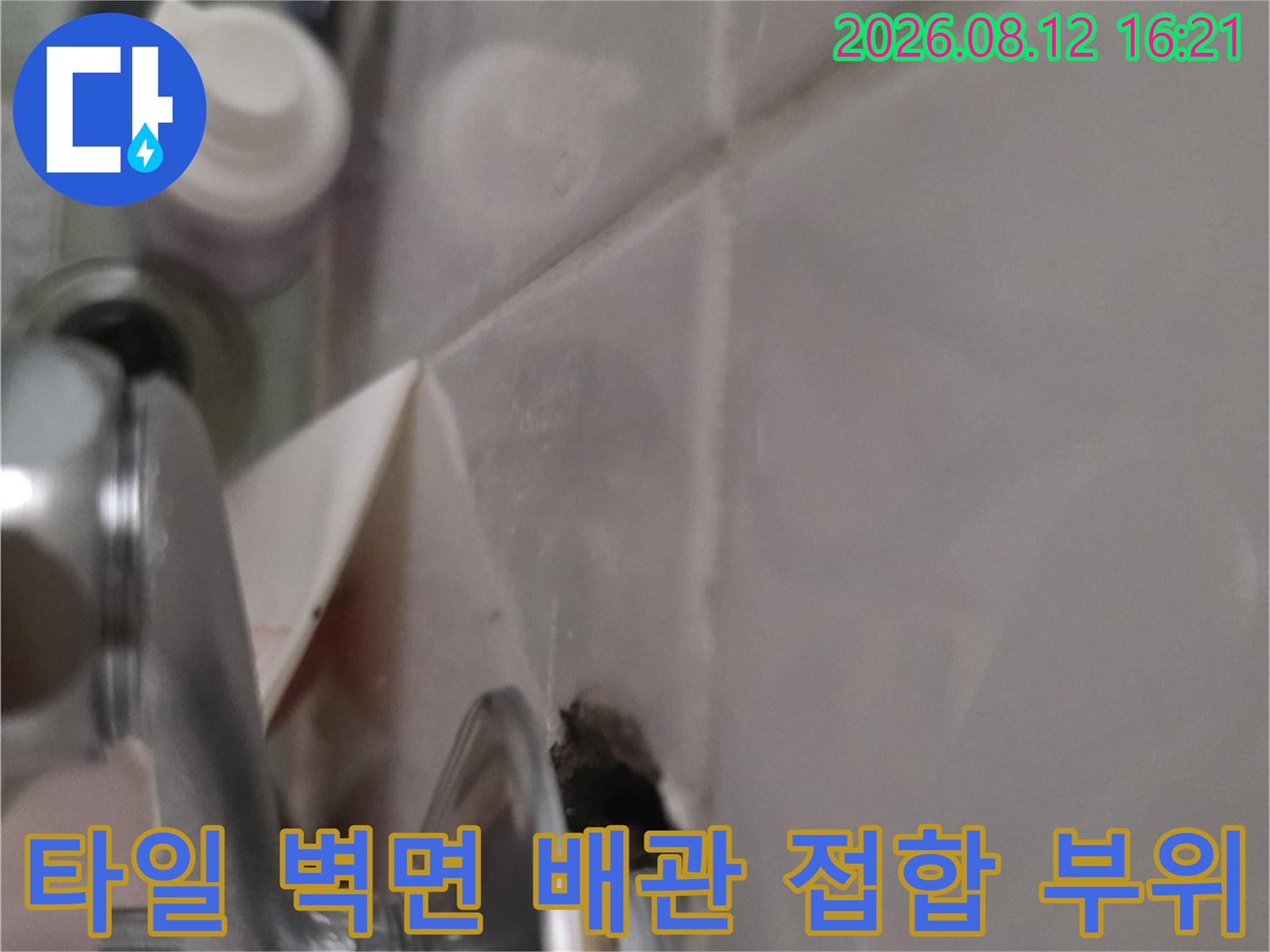 흰색 타일 벽면에 고정된 세면대 금속-배관 연결 지점의 확대 사진
