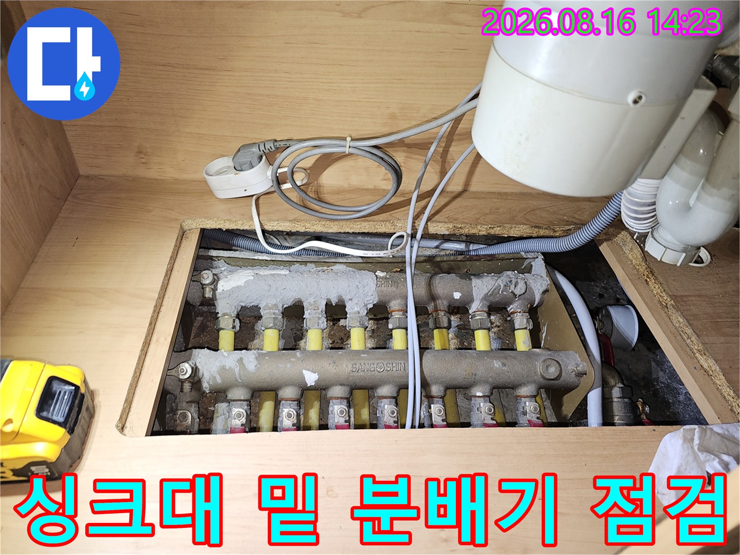 싱크대 하부장 내부의 보일러 분배기와 연결 배관 상태를 점검하는 모습입니다.