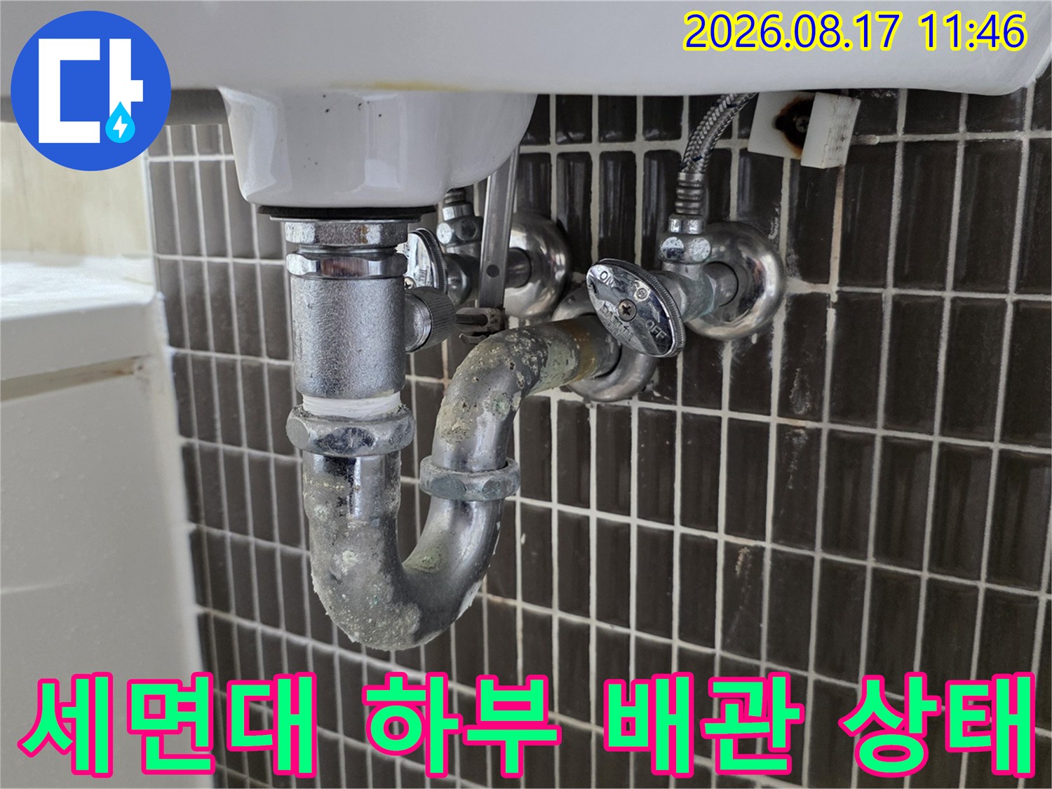 벽면 타일과 연결된 세면대 배수 트랩 및 급수 밸브 사진입니다.