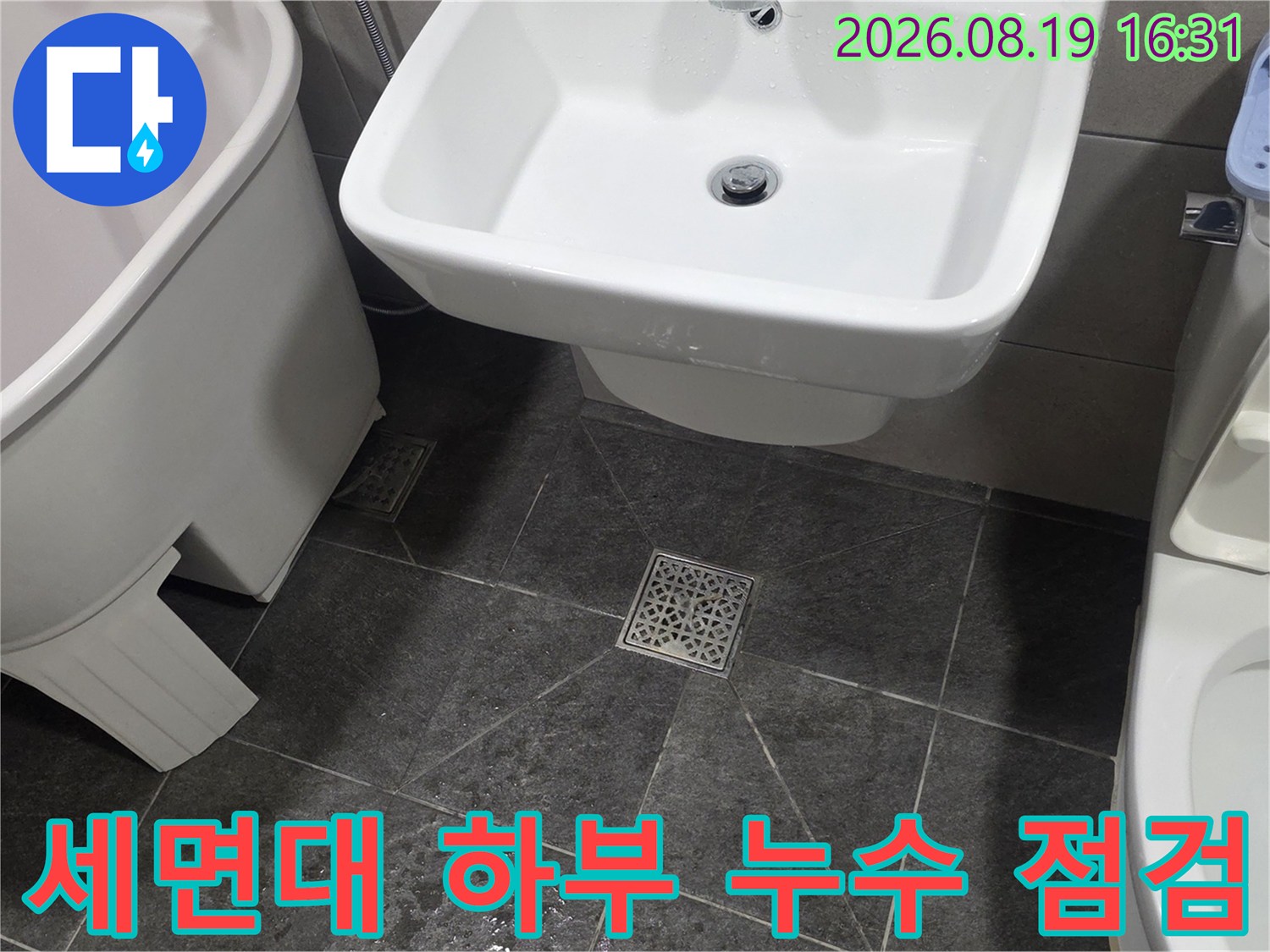 세면대 밑 배수구 주변과 바닥 타일의 물 고임 상태를 보여주는 사진입니다.