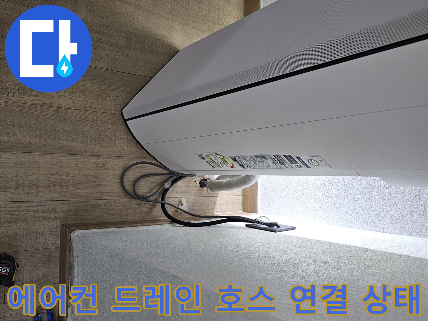 벽면과 에어컨 사이의 배수 호스가 어떻게 배치되어 있는지 보여주는 사진입니다.