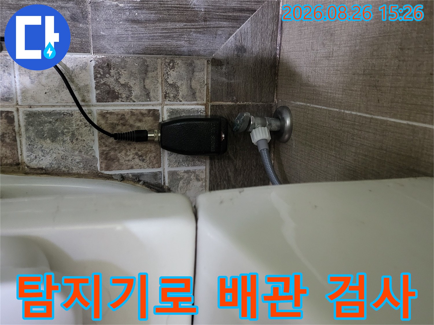변기 하단 급수 밸브와 연결된 배관에 누수 탐지용 센서를 부착하여 점검하는 장면입니다.