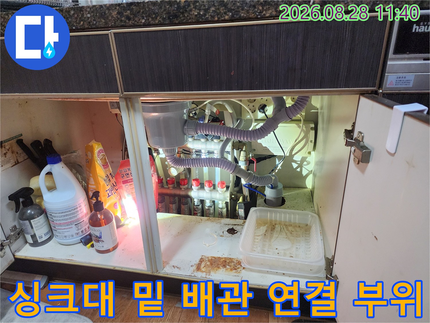 싱크대 하부장 내부의 복잡하게 얽힌 배수 호스 및 드레인 라인