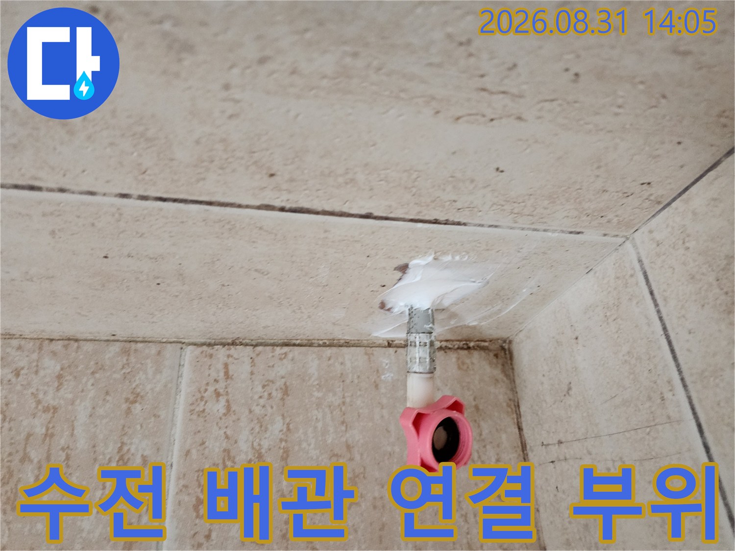 타일 벽면에 돌출된 분홍색 밸브와 은색 수도 배관의 모습입니다.