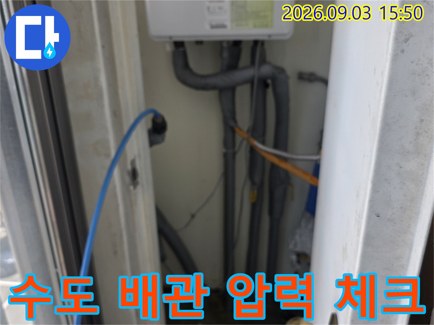 하얀색 계량기함 근처의 복잡한 배관들과 연결된 파란 호스