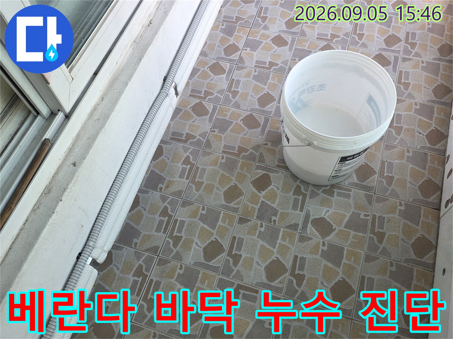 베란다 타일 사이의 균열과 배관 주변 마감 상태를 상세히 관찰하고 있습니다.