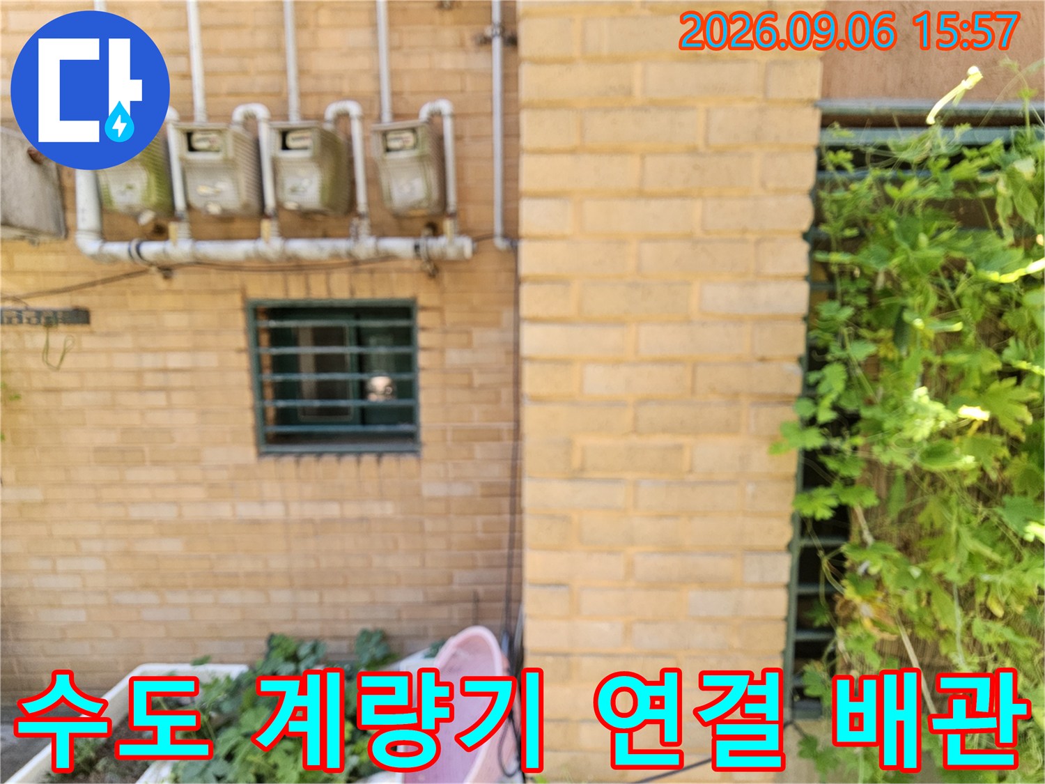 벽면에 설치된 수도 계량기와 외부로 연결된 흰색 배관의 근접 사진입니다.