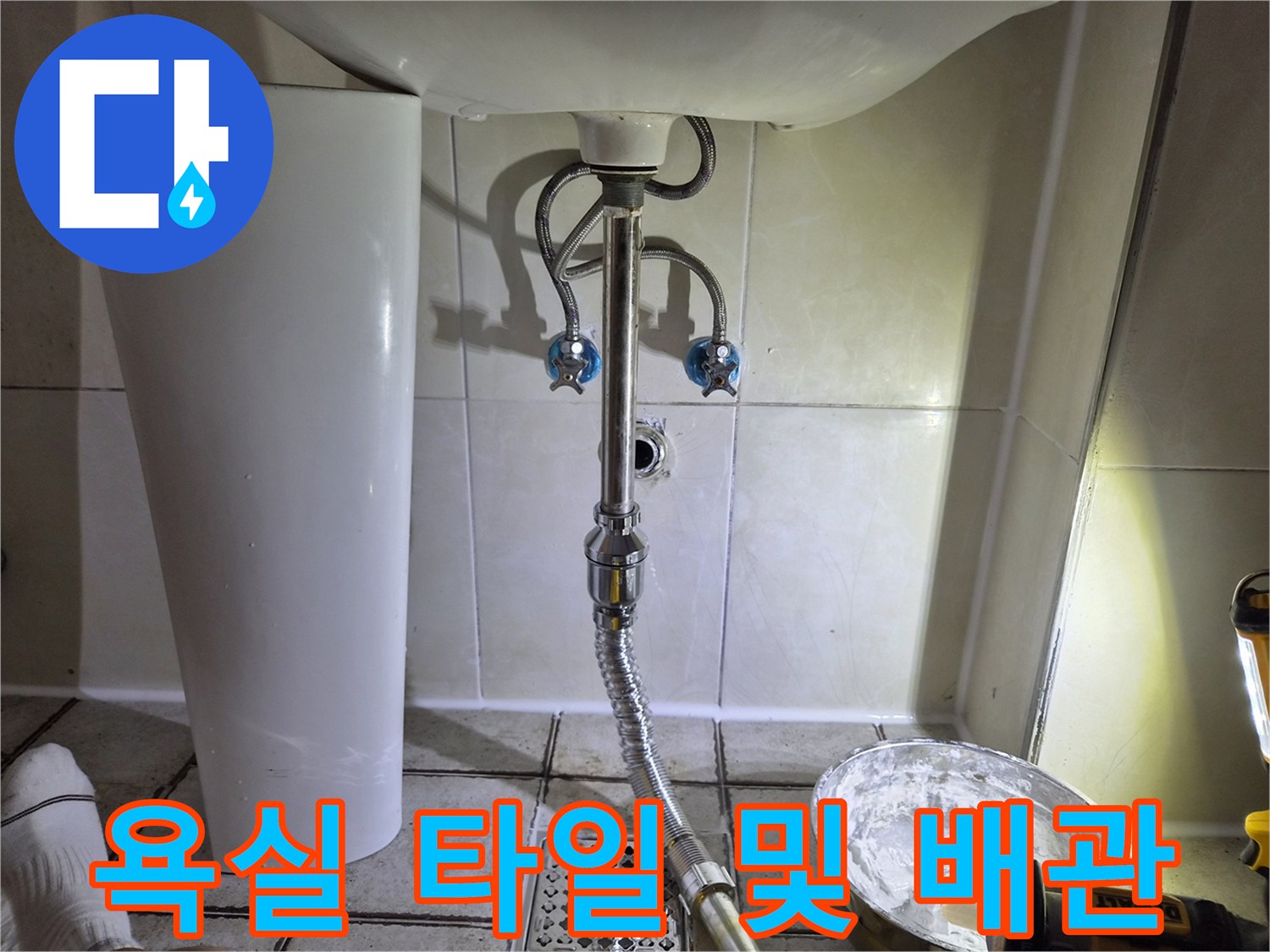 세면대 아래쪽 은색 배수 호스와 흰색 벽면 타일
