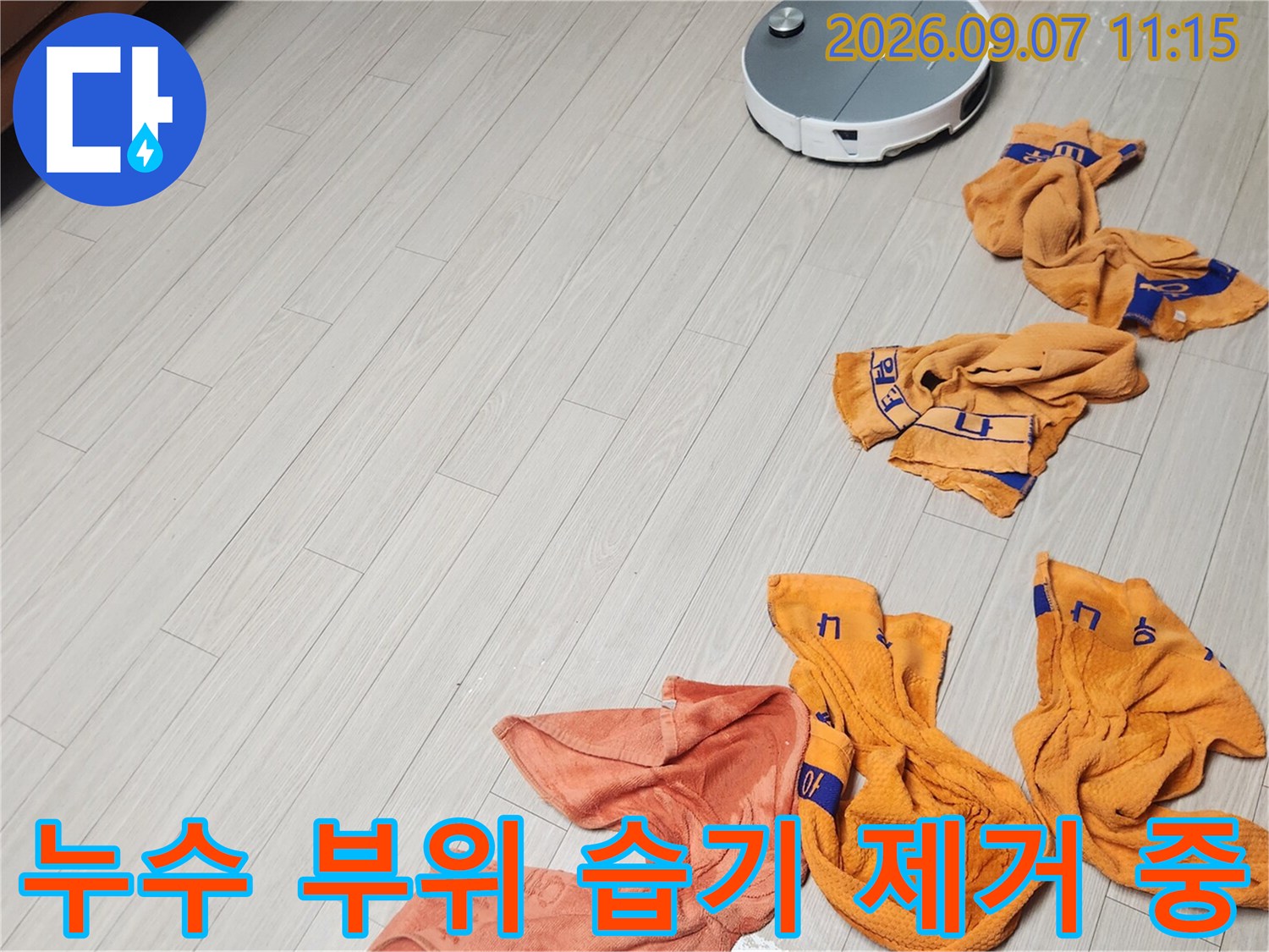 누수가 의심되는 바닥의 물기를 수건으로 닦아내는 작업 현장입니다.