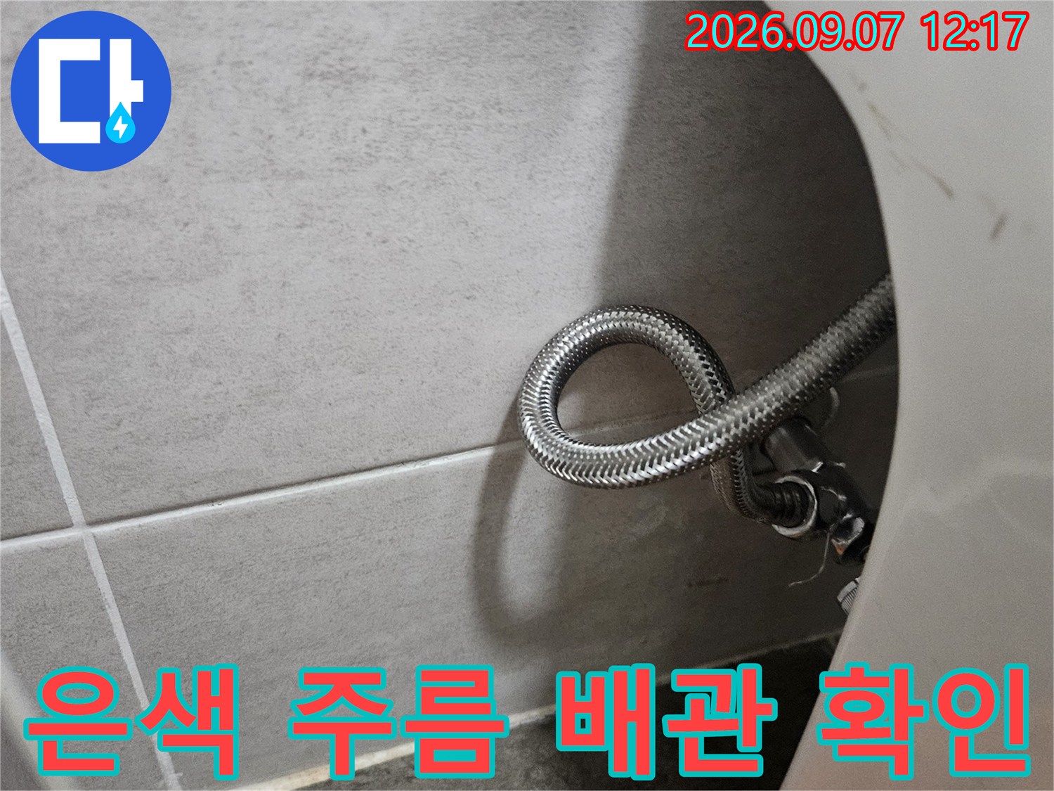 싱크대 밑에 둥글게 말린 은색 금속 재질의 호스