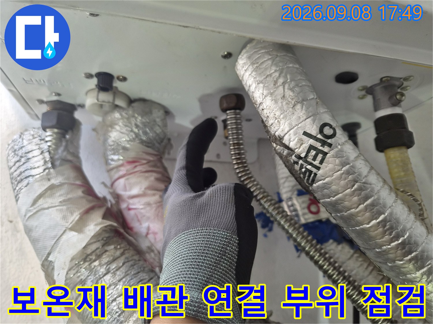 은색 보온재가 씌워진 배관과 금속제 연결 부품을 검사하는 장면입니다.