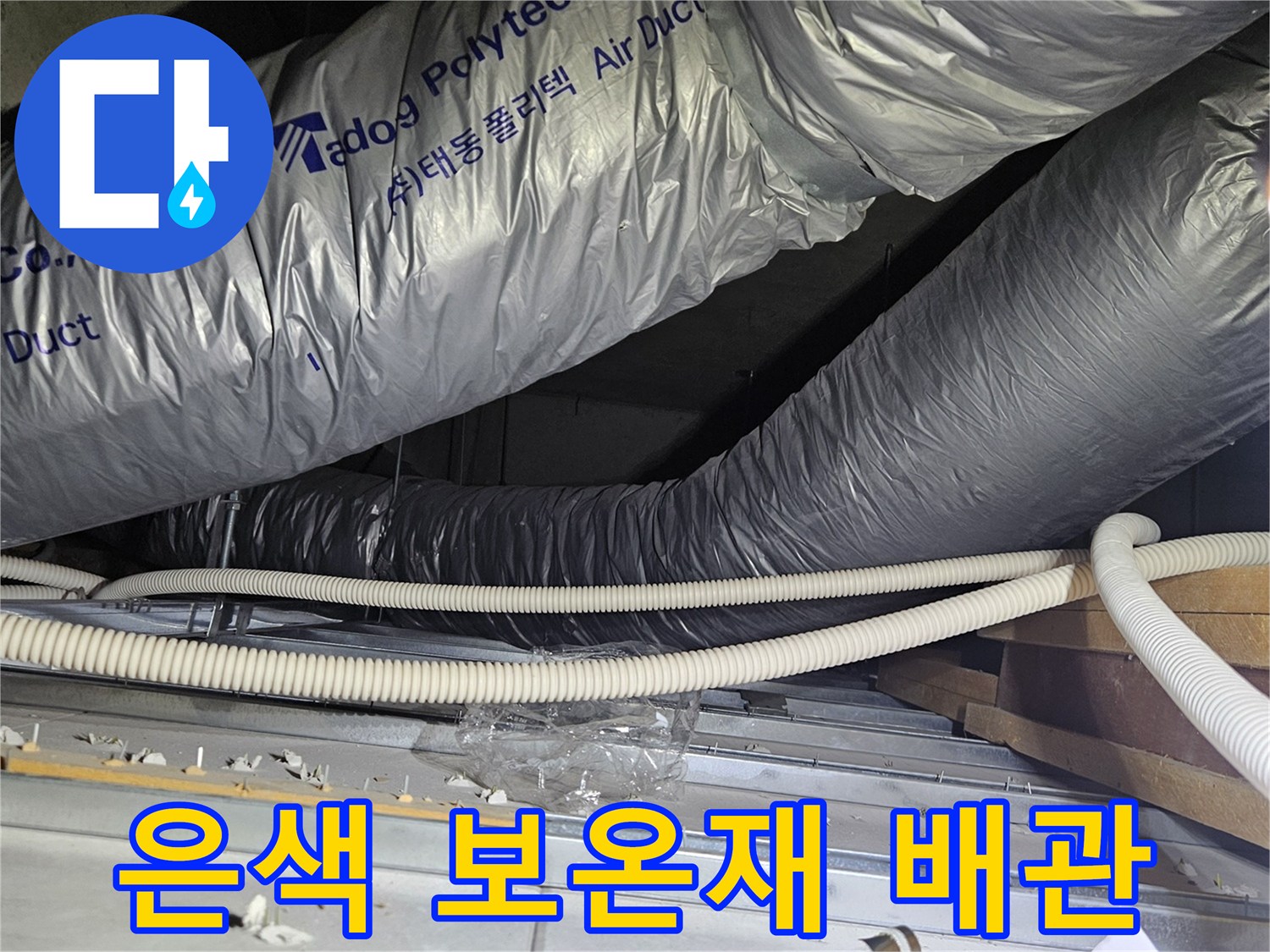 보온재로 마감된 은색 덕트와 하얀색 전선용 호스가 지나가는 배관 구조입니다.