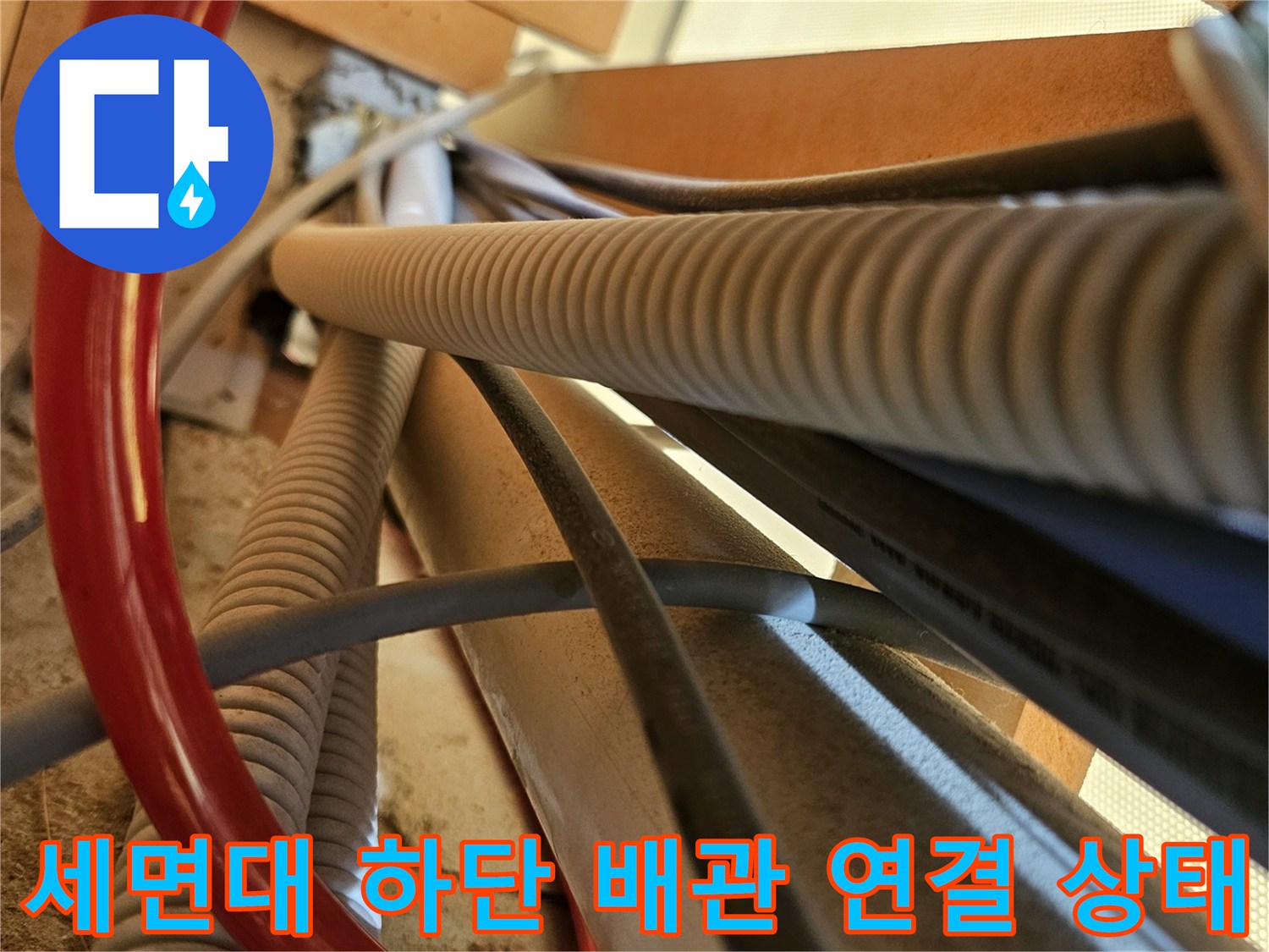 붉은색 호스와 회색 주름관이 얽힌 세면대 하부 배관