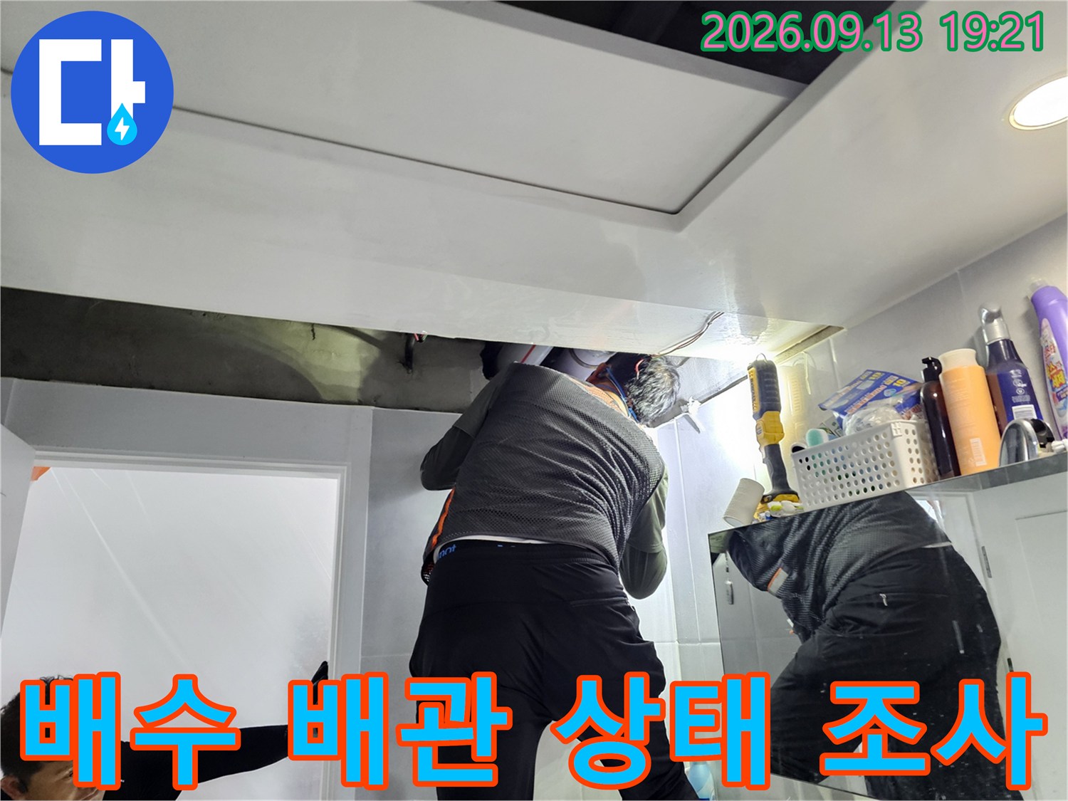 욕실 천장 내부의-배수관 연결 부위를 조명으로 밝혀 점검하는 현장입니다.