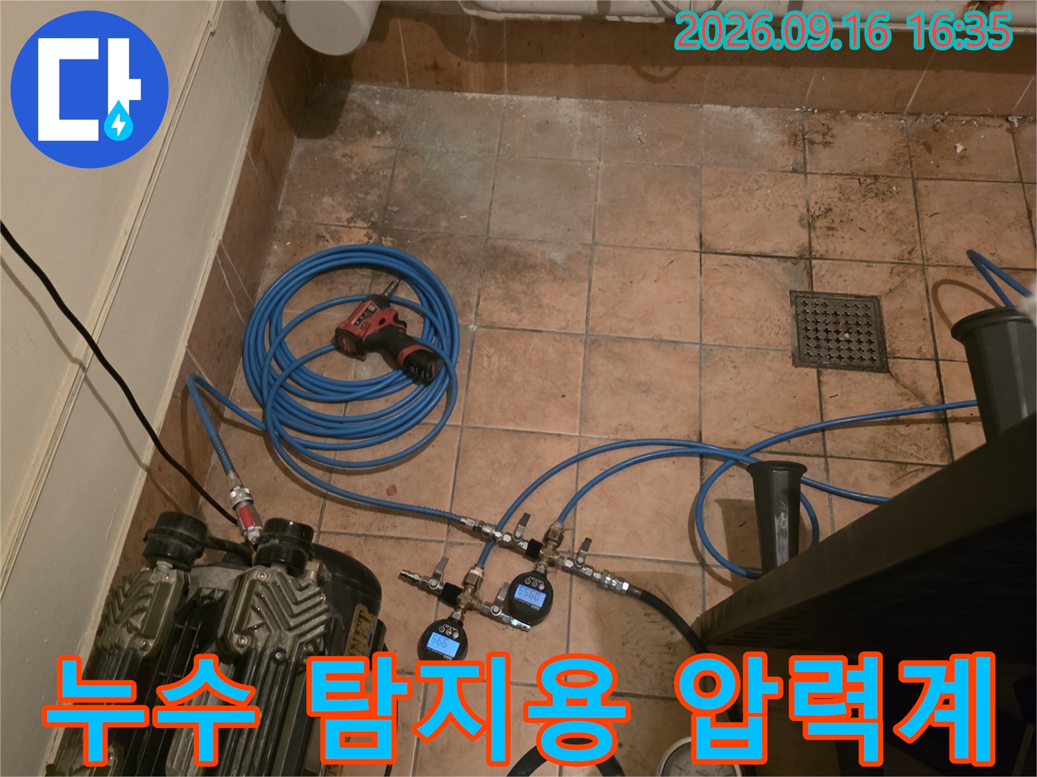 바닥 타일 위에 놓인 누수 탐지를 위한 압력 게이지와 각종 배관 연결 장비들
