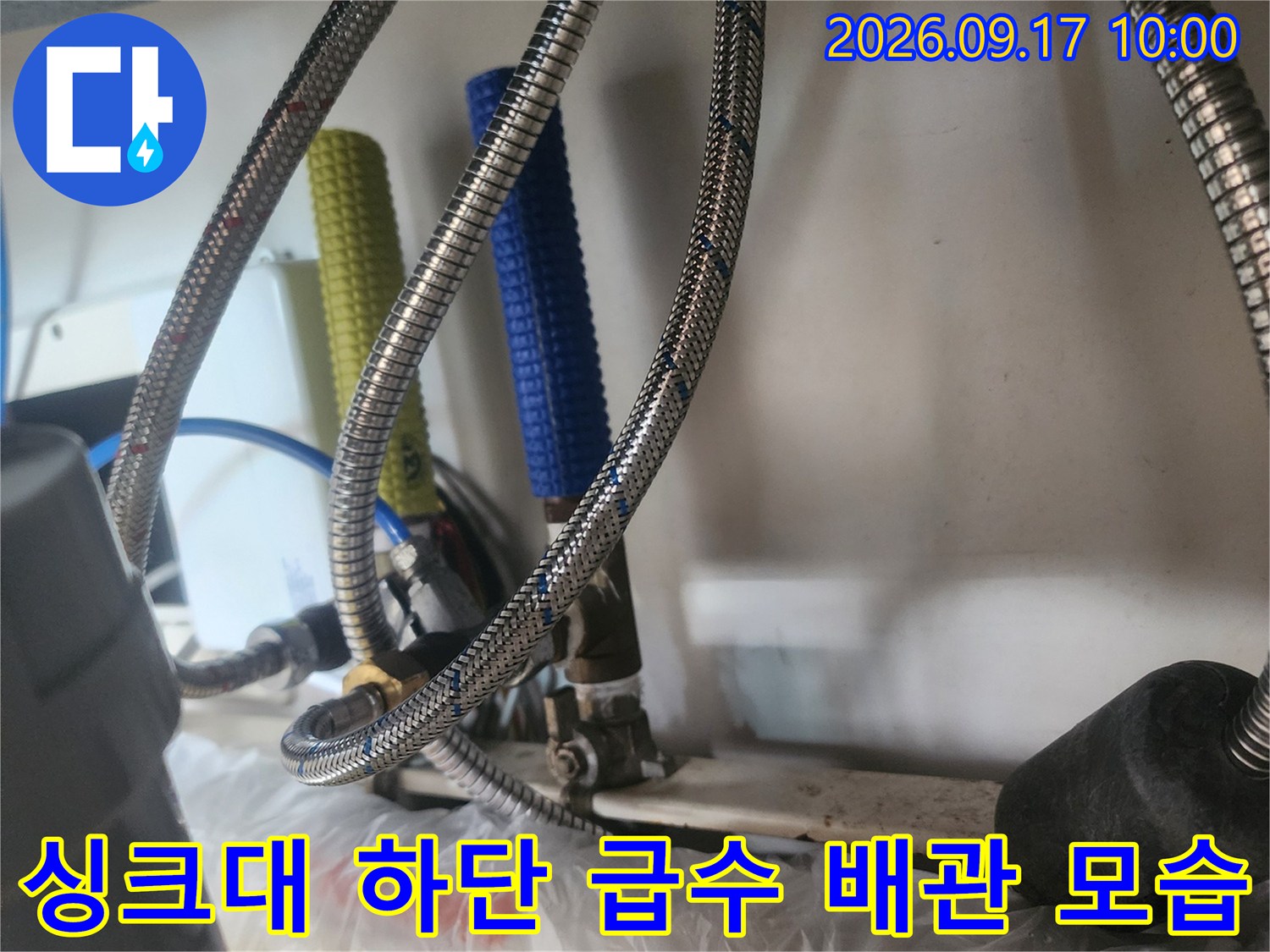 은색 호스와 파란색 튜브가 연결된 싱크대 밑부분의 사진입니다.