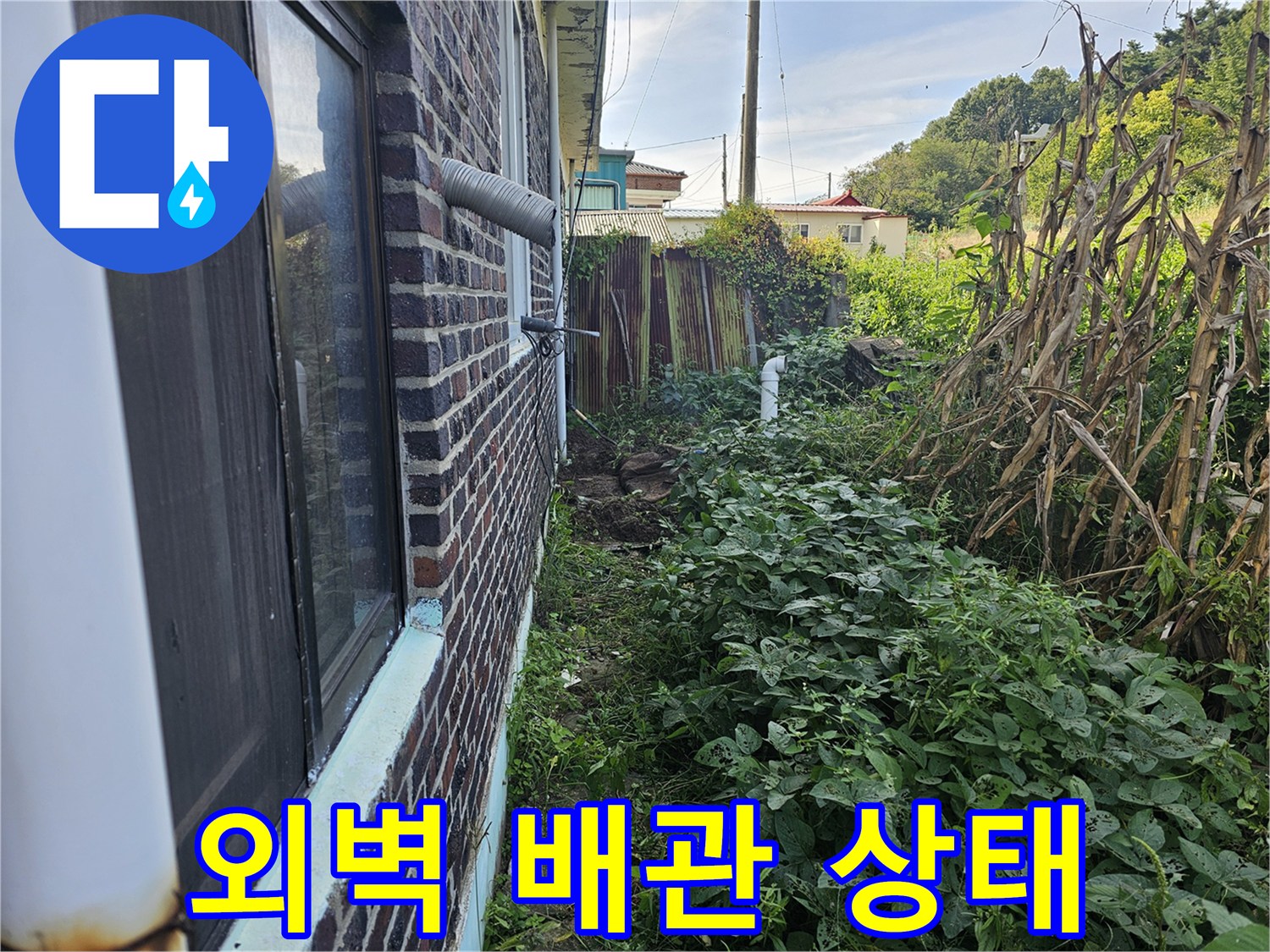 붉은 벽돌 외벽과 은색 금속 배관-주변 잡초가 무성한 현장